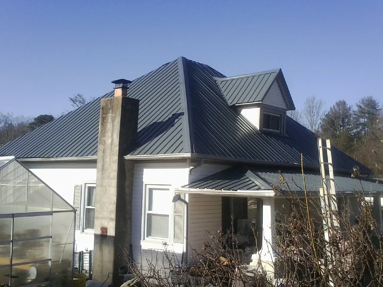 Dark blue standing seam metal roof on a white farmhouse with dormer — Slate & Tile Roof Repair by Roofing Brothers in Wilkesboro
