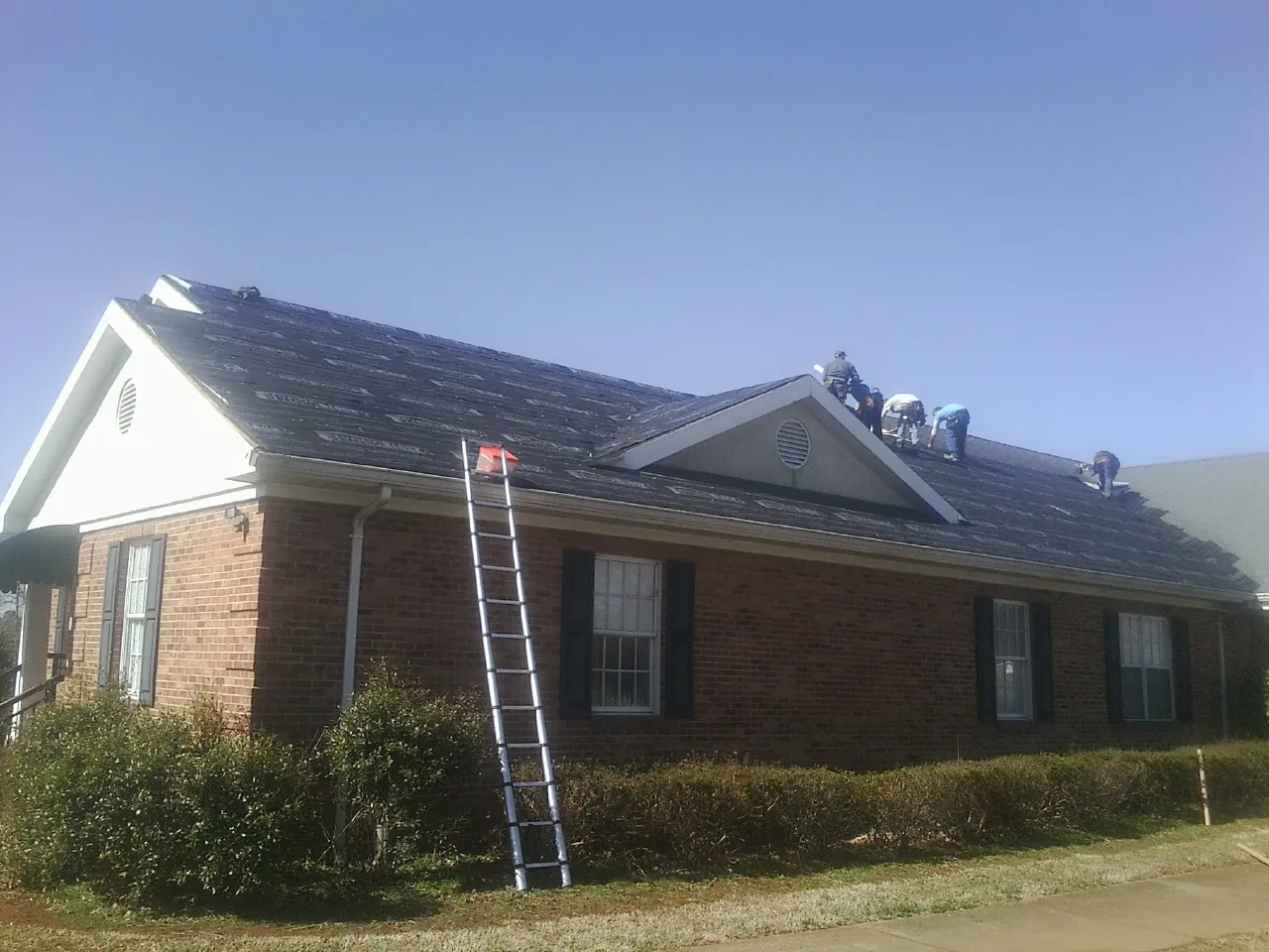 Crew tearing shingles off a brick ranch roof with a ladder set — Metal Roof Repair work by our crew in Wilkesboro