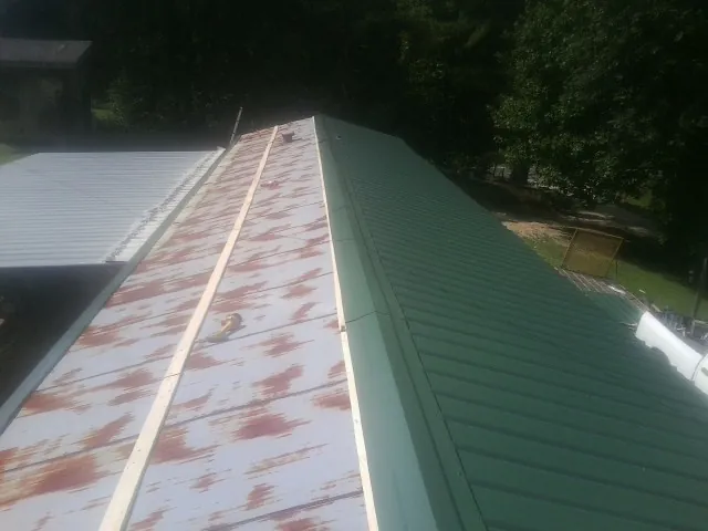 Old rusted panels beside newly installed green metal roofing — Wind Damage Roof Repair by Roofing Brothers in Wilkesboro
