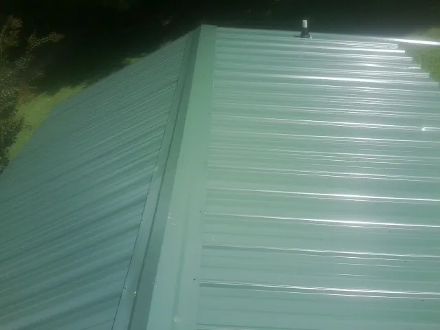 New green metal panels meeting at the ridge of a roof — Flat Roof Repair work by our crew in Wilkesboro