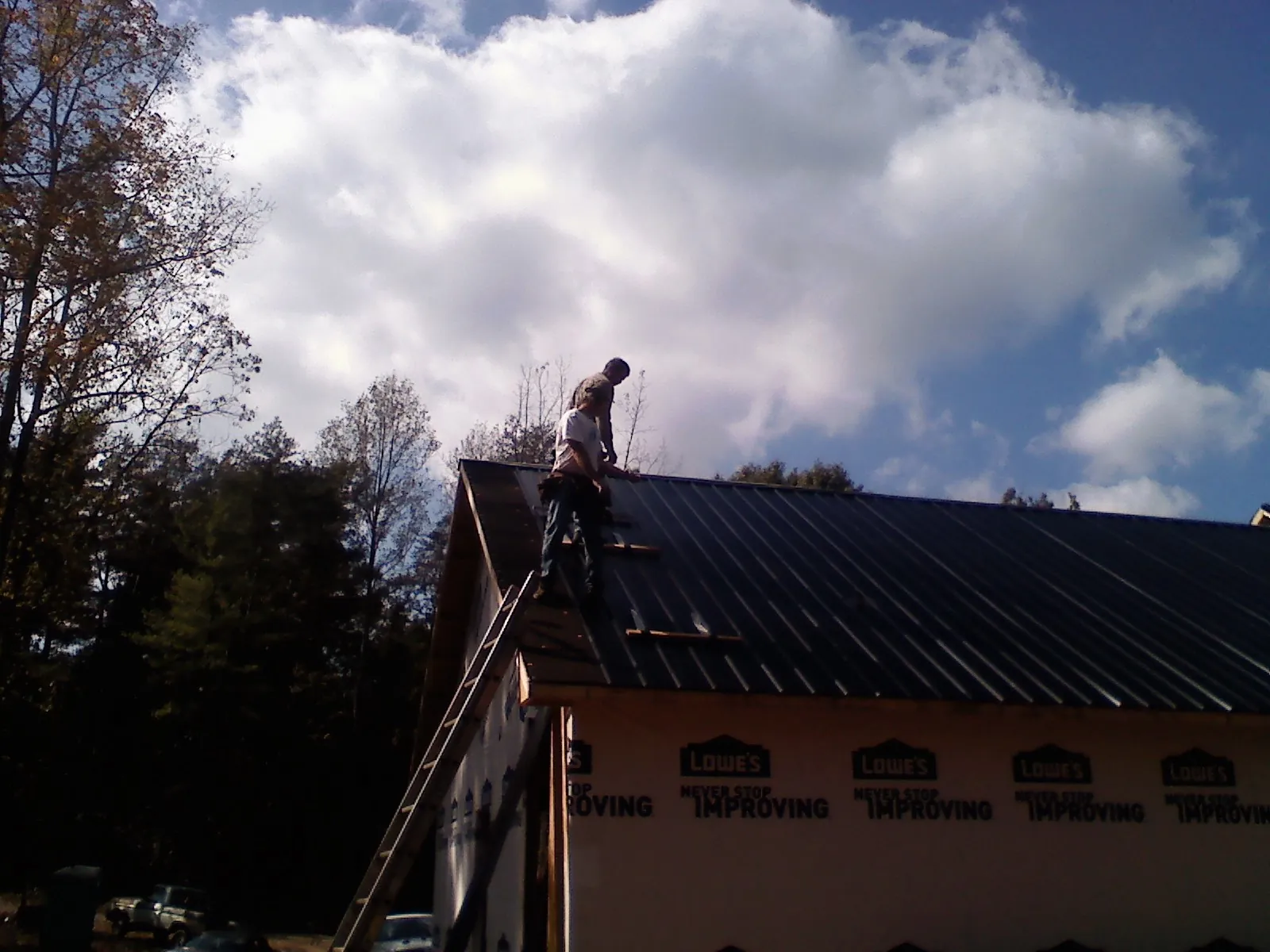 Roofer fastening dark metal panels high against a cloudy sky, from a Roof Inspection job in Wilkesboro