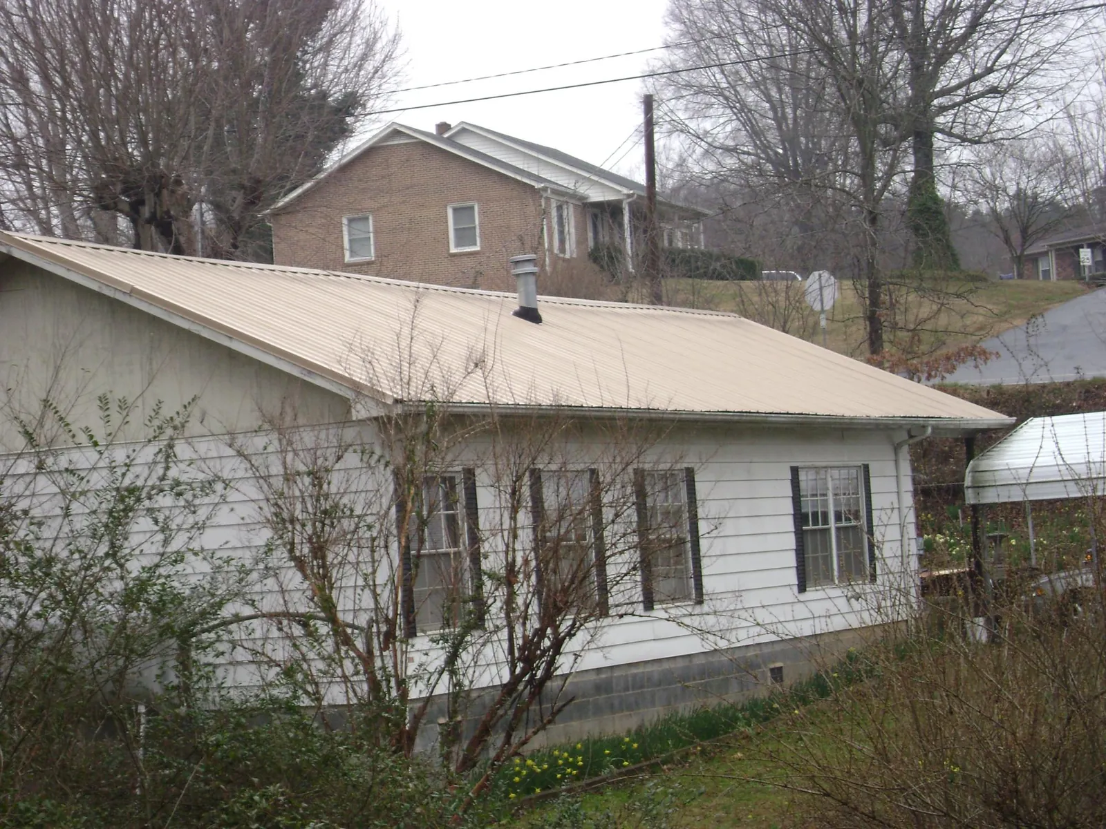 Tan metal roof on a white sided house set into a hillside — Commercial Roofing by Roofing Brothers in Wilkesboro